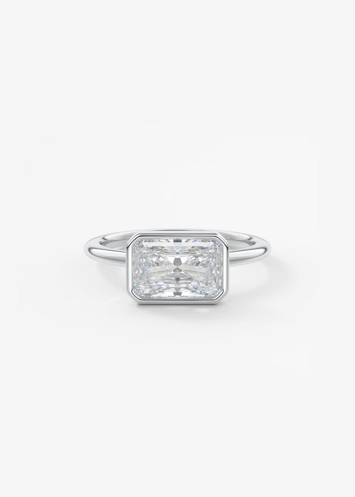 An emerald-cut diamond engagement ring in a silver-toned metal band, centered on a clean white background.#material_white