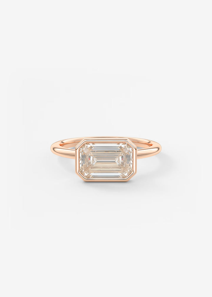 A rose gold ring featuring a large rectangular emerald-cut clear gemstone in a bezel setting, shown against a plain white background.#material_rose