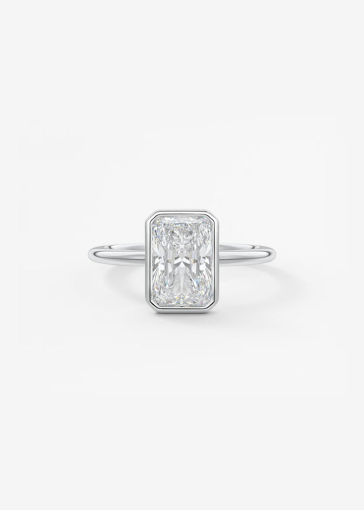 A silver-toned ring featuring a rectangular baguette-cut diamond center stone, shown on a clean white background.#material_white
