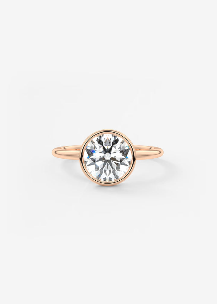 A rose gold engagement ring featuring a round brilliant-cut clear gemstone in a bezel setting, shown against a plain white background.#material_rose