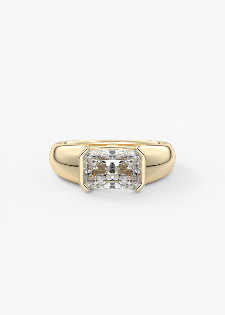 A yellow gold ring featuring a large, radiant-cut clear gemstone in a bezel setting, shown against a plain white background.#material_gold