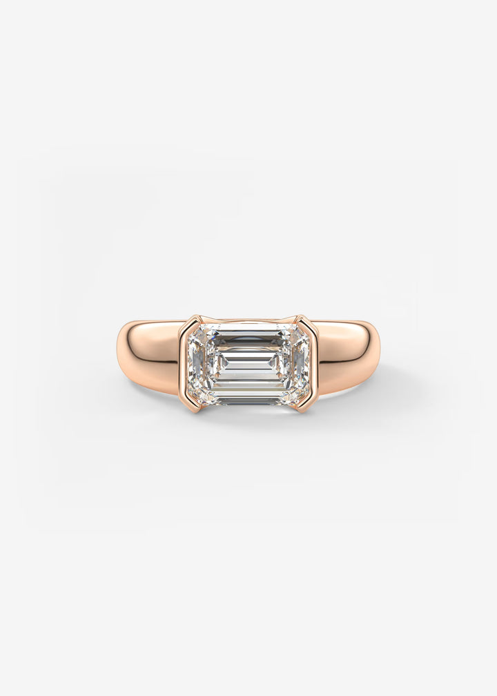 A rose gold ring featuring an emerald-cut clear gemstone in a four-prong setting, shown against a plain light gray background.#material_rose