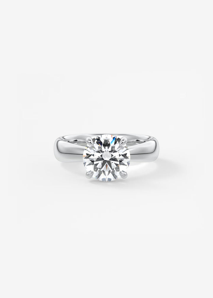A classic solitaire engagement ring featuring a round brilliant-cut diamond set in a polished silver-colored band, centered on a clean white background.#material_white