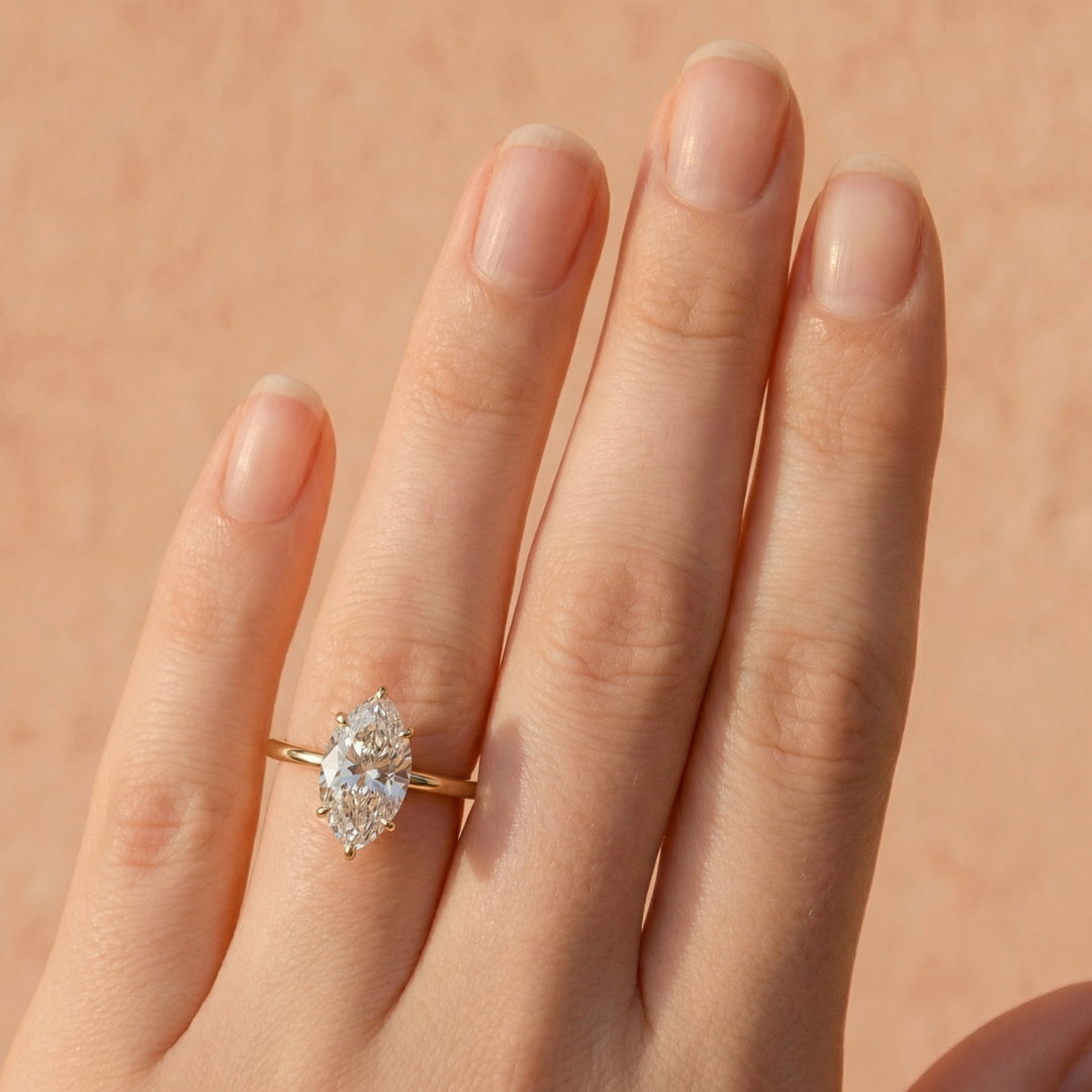 Gold ring with a diamond on a hand against a beige background #material_gold