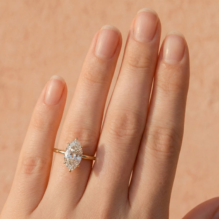 Gold ring with a diamond on a hand against a beige background #material_gold