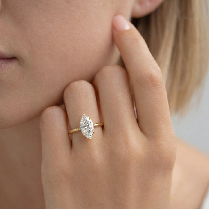 Close-up of a hand wearing a gold ring with a diamond, touching the cheek. #material_gold