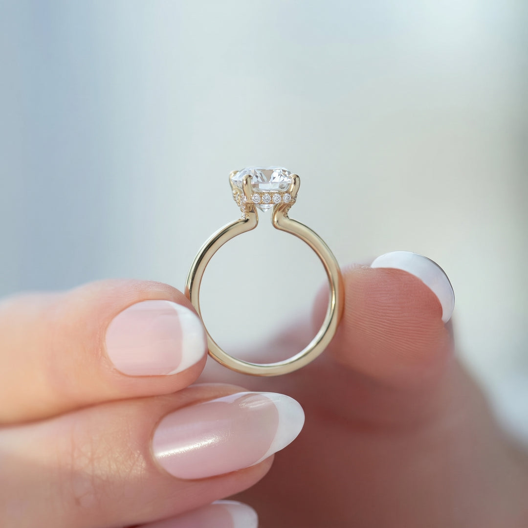 A close-up of a gold ring with a large clear center stone and small side stones, held between fingers with a soft blurred background. #material_gold