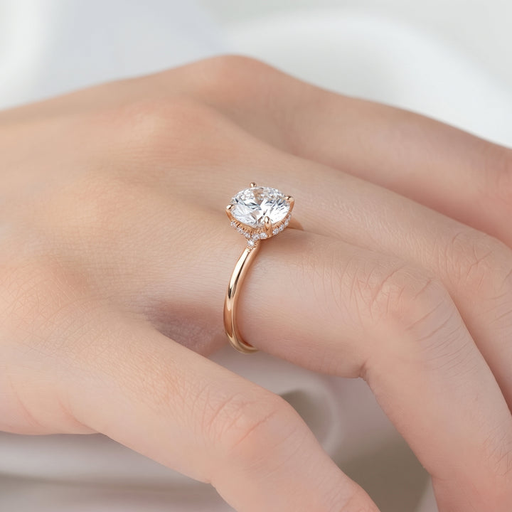A close-up of a hand wearing a rose gold ring with a marquise-cut clear gemstone and small accent stones, set against a soft, light background. #material_rose