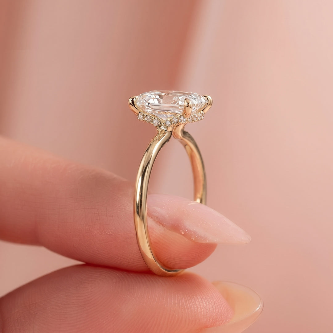A close-up of a gold ring with a large clear heart-shaped gemstone and small accent stones, held between fingers against a soft pink background. #material_gold