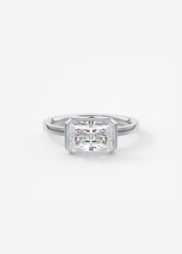 An emerald-cut diamond engagement ring in a polished silver-colored metal band, centered on a clean white background.#material_white