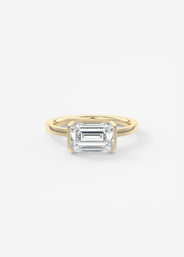A yellow gold ring featuring an emerald-cut clear gemstone, presented on a clean white background.#material_gold