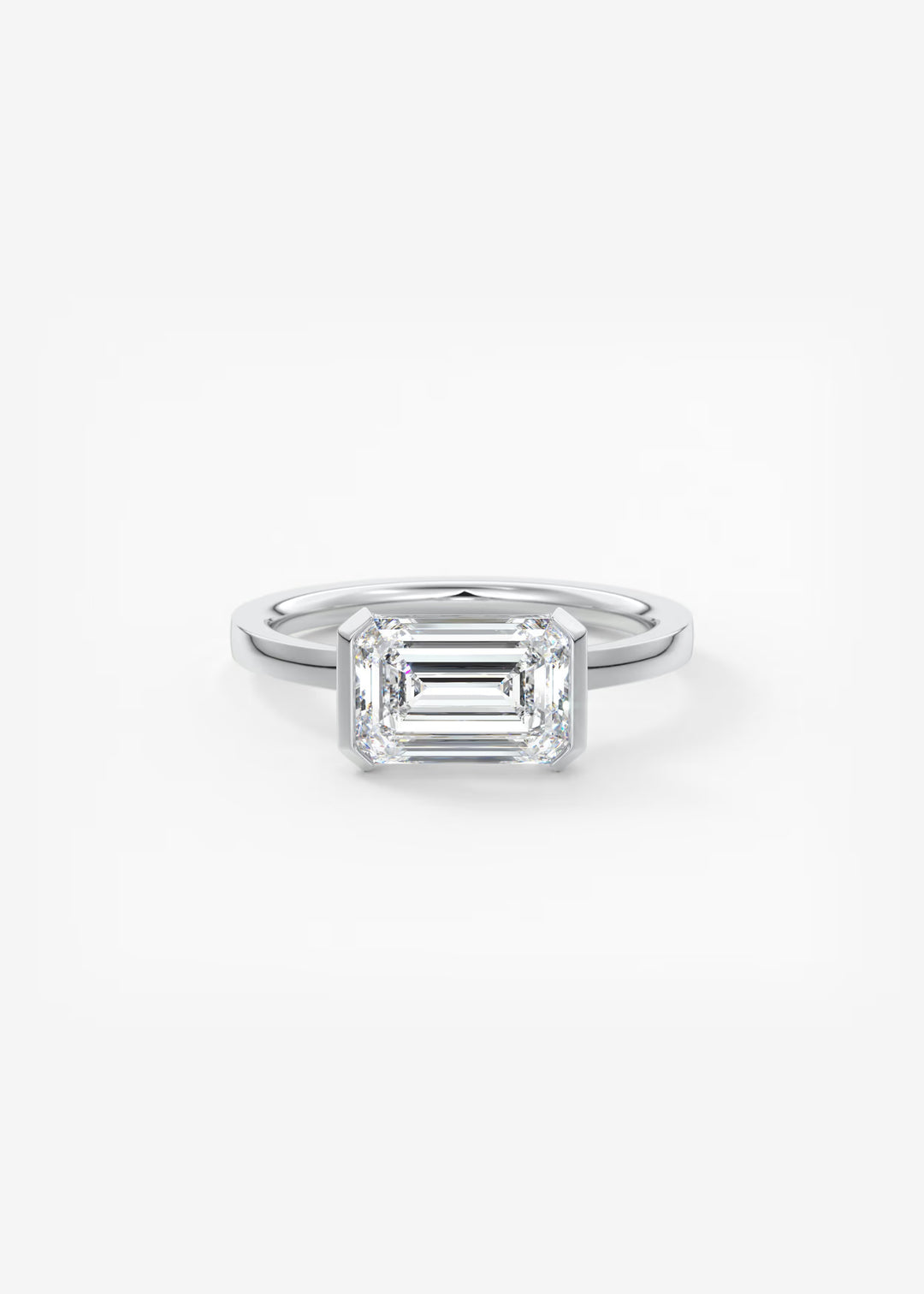 An emerald-cut diamond engagement ring in a silver-toned metal band, centered on a clean white background.#material_white